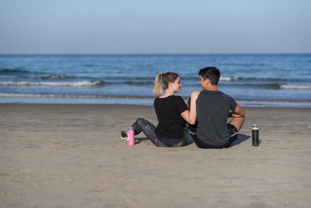 Young couple in love sitting on the rocky beach and looking on the horizon at sea. Lovestory concept. - Foto, imagen