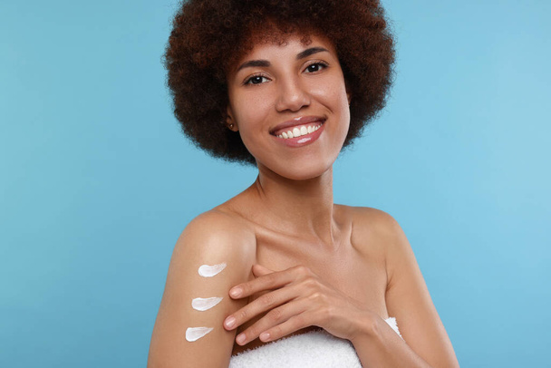 Beautiful young woman applying body cream onto arm on light blue background - Foto, Imagen