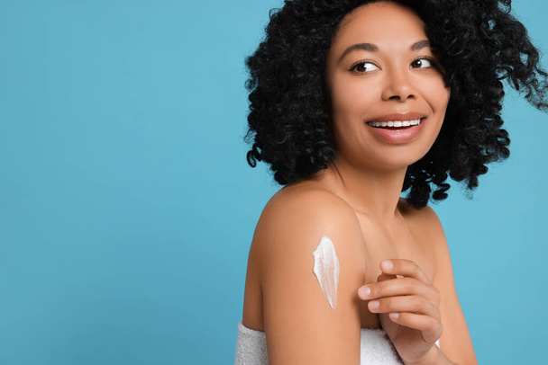 Young woman applying body cream onto shoulder on light blue background. Space for text - Foto, imagen