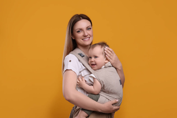 Mother holding her child in sling (baby carrier) on orange background - Fotoğraf, Görsel