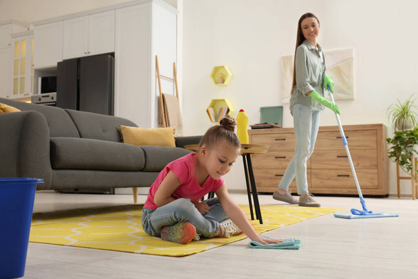 Spring cleaning. Mother and daughter tidying up living room together - Foto, imagen