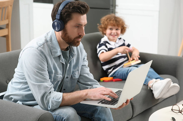 Отец работает удаленно на ноутбуке, пока его сын играет с игрушками дома - Фото, изображение
