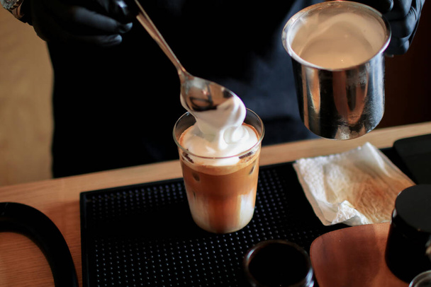 Barista pour milk foam on Ice cappuccino coffee. Cold summer drink.  Cold summer drink on a dark wooden background with copy space. - Foto, imagen