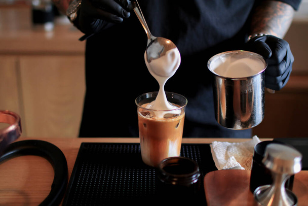 A barista tejhabot öntött a Ice cappuccino kávéra. Hideg nyári ital. Hideg nyári ital egy sötét fa háttér másolási hely. - Fotó, kép