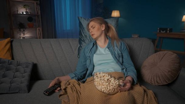 A fiatal nő elaludt a film alatt. Egy fáradt nő alszik, a kanapén ül, közelről, popcornnal az ölében, távirányítóval a kezében. Unalmas film - Fotó, kép