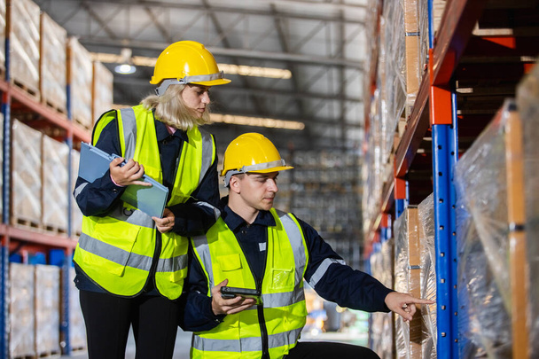 Male and Female professional worker wearing safety uniform and hard hat using digital tablet inspect product on shelves in warehouse. supervisor worker checklist stock inspecting product in factory. - Zdjęcie, obraz