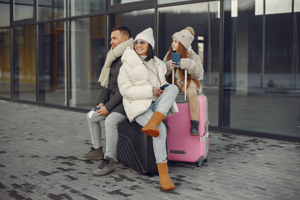 Family of three going on vacation. Man and woman sitting on a luggage and holding passports. Mother, father and daughter wearing warm clothes. - Foto, imagen