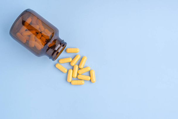 Stapel van een aantal gele capsule pillen buiten een glazen fles op een lichtblauwe achtergrond. Ruimte voor tekst. Begrip geneesmiddel en behandeling. - Foto, afbeelding