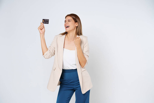 Kredi kartı tutan ve başarıyı kutlayan heyecanlı genç kadın beyaz arka planda izole edilmiş.. - Fotoğraf, Görsel