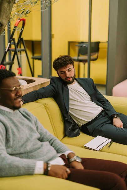 Dobře vypadající různí lidé sedí na žluté pohovce v kanceláři a berou pauzu formou práce - Fotografie, Obrázek