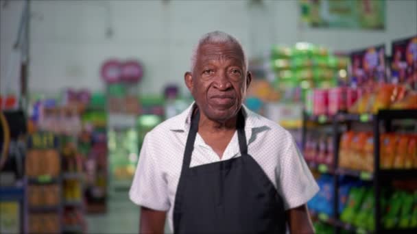 Нейтральний вираз Портрет старшого афроамериканського співробітника в супермаркеті, що стоїть з фартухом - Кадри, відео