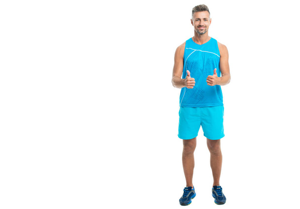 Sport and healthy lifestyle. full length of athlete. confident athlete wearing sport wear showing thumb up. The male sport athlete posing on studio. sport athlete with fit body isolated against white. - Foto, Imagen