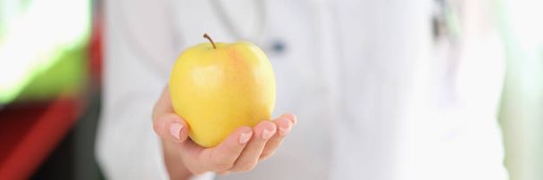 Close-up of female doctor nutritionist holding ripe yellow apple in hand. Healthy food, diet, vitamins and balanced nutrition concept - Zdjęcie, obraz