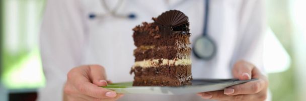 Zbliżenie kobiecego dietetyka trzymającego w rękach kawałek ciasta czekoladowego. Zdrowa żywność, dieta, zrównoważone odżywianie i koncepcja diety - Zdjęcie, obraz