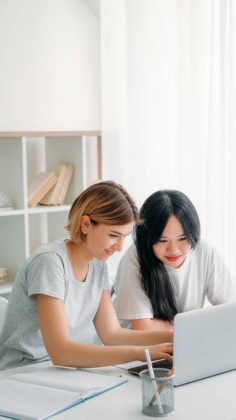 Studying teamwork. Learning cooperation. Homework together. Two happy young girls typing on laptop browsing internet for school research project at home workplace. - 写真・画像