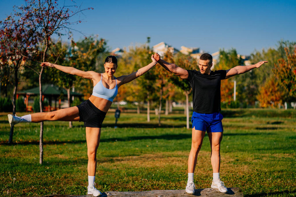 Sporty couple standing on a tree. A handsome man is supporting his girlfriend to stretch her legs - Fotografie, Obrázek