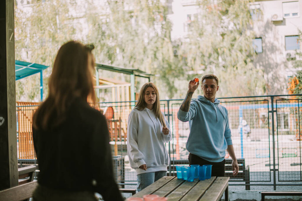 Friends playing beer pong while standing at the park - Фото, изображение