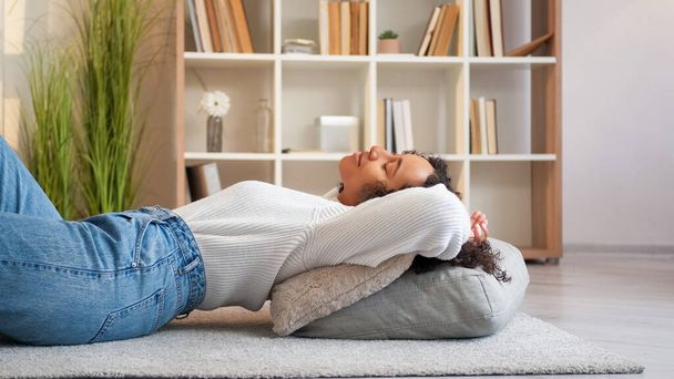 Home relax. Rest indoors. Lazy weekend. Peaceful serene cheerful woman lying on floor comfortable cushions at cozy living room. - Fotó, kép