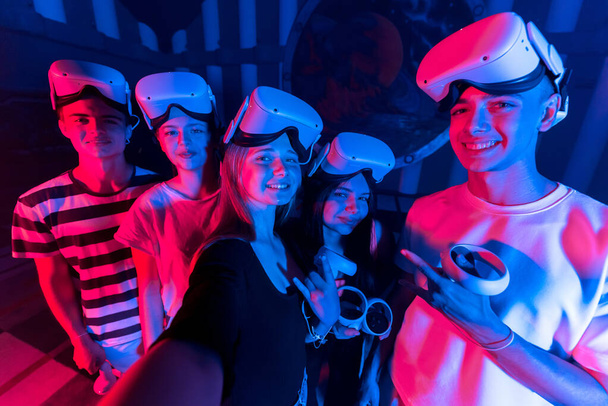 A team of young friends taking selfie while using virtual reality VR equipment on an arena. Neon lights - Photo, image