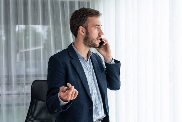 Hardworking businessman stand confidently in modern office making persuasive sales call to client. Office worker talking on the phone coordinate and manage business work with colleagues. Entity - Photo, Image