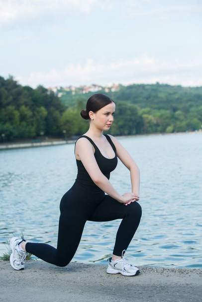 Young woman in black sportswear exercising outdoors. Fitness and healthy lifestyle concept. The white girl does sports in the park. - Valokuva, kuva