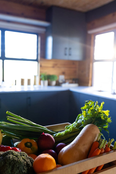 Vertical image of crate of organic vegetables on countertop in sunny kitchen in log cabin. Food, nutrition, balanced diet and healthy living. - Foto, immagini