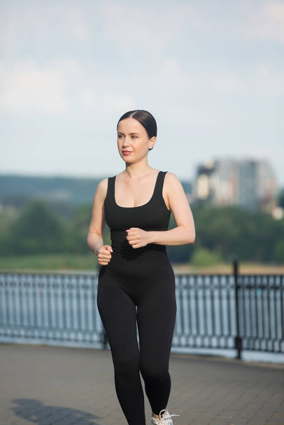 Young woman in black sportswear exercising outdoors. Fitness and healthy lifestyle concept. The white girl does sports in the park. - Foto, Imagem