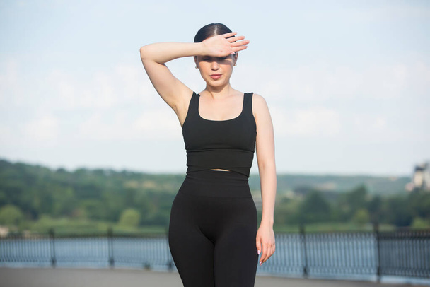 Young woman in black sportswear exercising outdoors. Fitness and healthy lifestyle concept. The white girl does sports in the park. - Photo, Image
