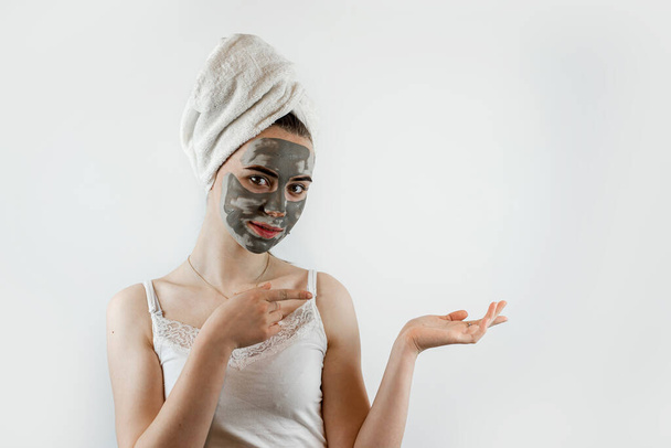 όμορφο κορίτσι με πετσέτα εφαρμογή μαύρη μάσκα caly στο πρόσωπο, αντι γήρανση θεραπεία ομορφιάς που απομονώνονται σε λευκό γκρι. Φροντίδα δέρματος - Φωτογραφία, εικόνα