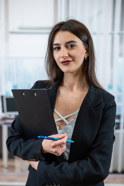 Single beautiful business woman in black suit holding paper doc standing in modern office. Successful female manager - Photo, Image