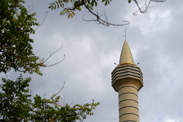Der Turm der Moschee, der sich hoch zwischen den Bäumen erhebt. - Foto, Bild