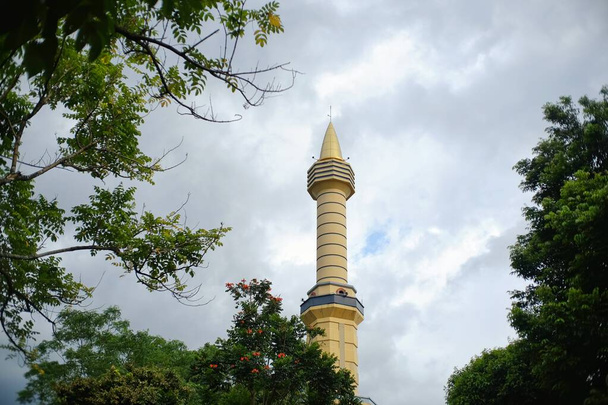 Башня мечети, которая возвышается высоко среди зеленых деревьев. Обычно используется для размещения громкоговорителей, чтобы призвать к молитве уведомление о времени молитвы. - Фото, изображение