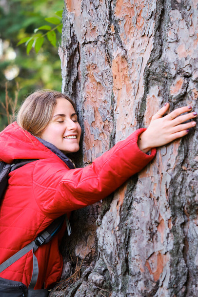 Sorridente giovane ambientalista femminile che abbraccia un albero nella foresta. - Foto, immagini