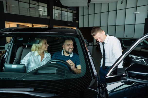 The seller demonstrates the interior of the car to buyers. Caucasian couple chooses a car - Valokuva, kuva