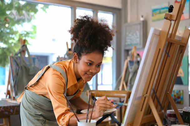 Ταλαντούχος Αφρο-Αμερικανός γυναίκα καλλιτέχνης δημιουργώντας αριστούργημα, ζωγραφική εικόνα με πινέλο σε καμβά στο στούντιο τέχνης. - Φωτογραφία, εικόνα