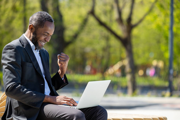 Working outside. African american businessman working on laptop in the park and looking contented - Foto, imagen