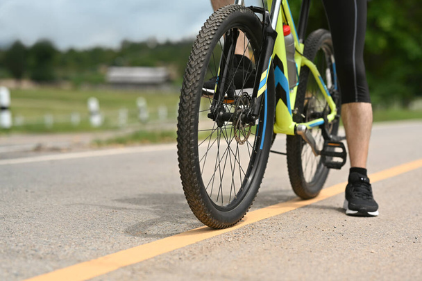 Ausgeschnittenes Bild eines sportlichen Mannes, der mit dem Fahrrad den Radweg in einem Stadtpark entlangfährt. Reise-, Sport- und Lifestylekonzept. - Foto, Bild