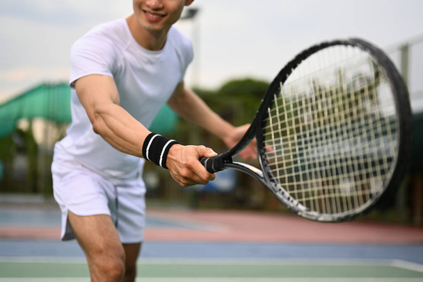 Hombre musculoso sonriente golpeando la pelota con raqueta para devolver la pelota sobre la red. Deporte, fitness, entrenamiento y concepto de vida activa. - Foto, Imagen
