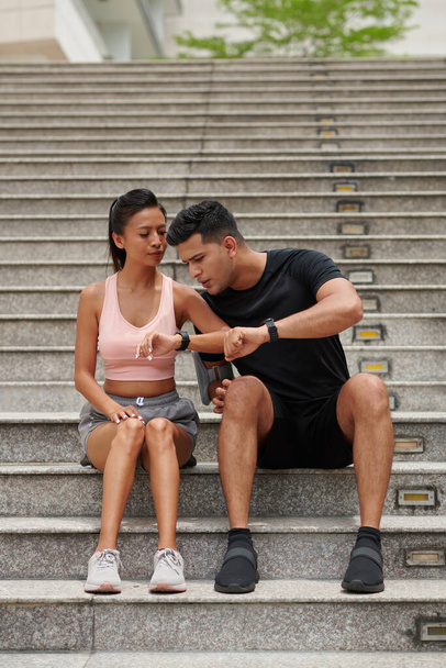 Přizpůsobit mladý muž porovnávání čísel v jeho a přítelkyně fitness trackers - Fotografie, Obrázek