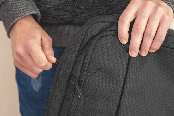 Κοντινό πλάνο. Τα χέρια των ανδρών στερεώνουν μια τσάντα. έναν προστατευτικό φάκελο για φορητό υπολογιστή. Ο τύπος κλείνει την τσάντα.  - Φωτογραφία, εικόνα