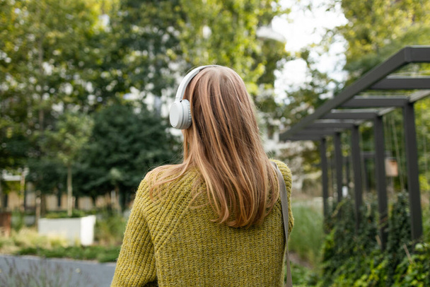 Nuori blondi valkoihoinen nainen kuuntelee musiikkia kävellessään kaupungin läpi. Laadukas kuva - Valokuva, kuva
