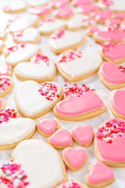 Herzförmige Zuckerkekse zum Valentinstag mit rosa und weißem Zuckerguss verzieren. - Foto, Bild