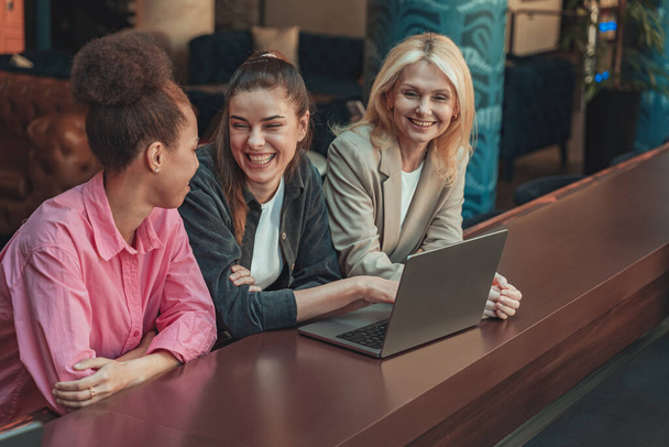 Τρεις γυναίκες συνάδελφοι κάθονται γραφείο με φορητό υπολογιστή και μιλάμε κατά τη διάρκεια του διαλείμματος. Υψηλής ποιότητας φωτογραφία - Φωτογραφία, εικόνα