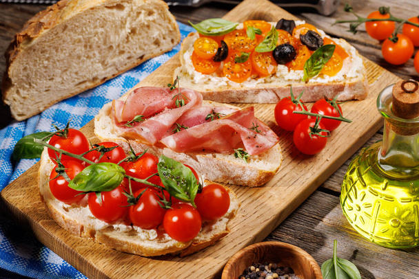 Восхитительный сэндвич с брускеттой, украшенный сочными помидорами, сыром и вкусной ветчиной на открытом столе в саду - Фото, изображение