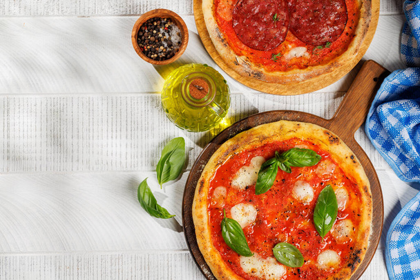 Homemade margarita and pepperoni pizza, topped with fresh tomatoes, mozzarella cheese, and aromatic basil leaves. On outdoor garden table flat lay with copy space - Photo, Image