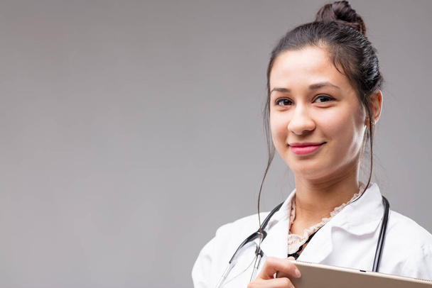Kopf- und Schulterschuss einer schönen philippinischen Ärztin, sie lächelt beruhigend mit ihrem digitalen Tablet. Es ist ein Werkzeug zur Verbesserung der Fähigkeiten von Chirurgen und Diagnostikern mit sofortiger Kommunikation und Datenzugriff - Foto, Bild