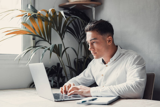красивый молодой бизнесмен с ноутбуком за столом, мужчина печатает руками на клавиатуре  - Фото, изображение
