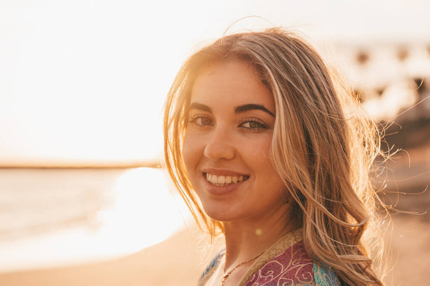 feliz sorrindo mulher loira posando na câmera na praia, pôr do sol céu e mar borrado no fundo  - Foto, Imagem