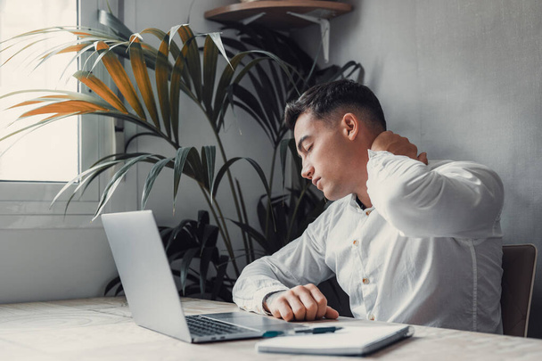 Уставший и уставший человек за столом с ноутбуком. бизнесмен с головным убором - Фото, изображение