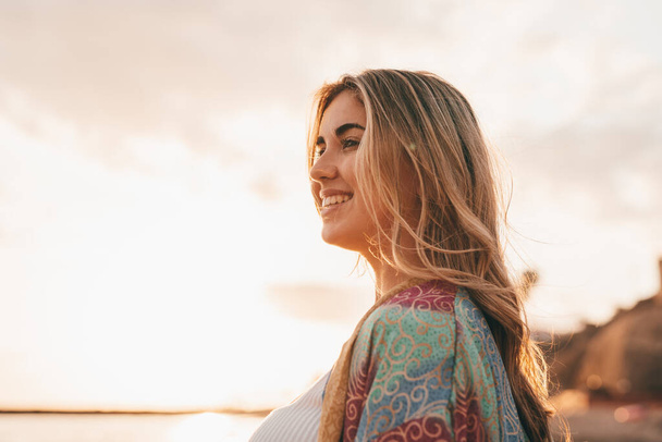 happy blonde woman at beach, sunset sky and blurred sea on background  - Photo, Image